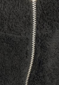 Chaqueta de forro polar negra con un prominente zipper plateado en la parte delantera, que resalta un tejido suave y texturizado.