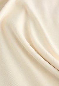 Material de culoare crem, cu o textură netedă și nervată, dispus în pliuri delicate. Linii fine și constante se întind pe întreaga suprafață.