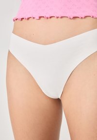 Tanga de algodón blanco con una textura suave y cintura en forma de V. Combinada con una blusa rosa con un patrón de corazones y dobladillo con volantes.