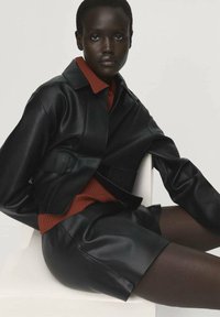 Zwarte leren cropped jack over een rode geribbelde trui en zwarte leren shorts. Gladde textuur, eenvoudig ontwerp, minimale detaillering.
