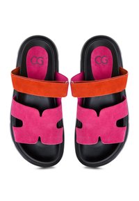 Sandales à glissière noires avec des brides avant en daim rose et des brides de cheville orange, présentant le logo CG sur les semelles roses.