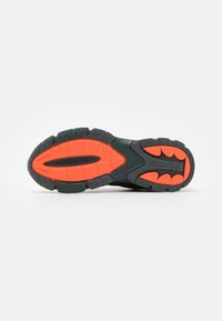A Lacoste sneaker talpa fekete gumialapú, jellegzetes narancs és szürke barázdákkal, kiemelkedő logóval és dinamikus, textúrált dizájn elemekkel rendelkezik.