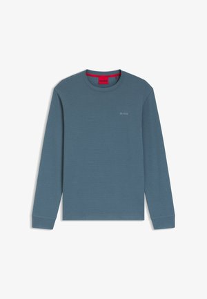 Niebieska koszula z długim rękawem wykonana z teksturowanego materiału, z okrągłym dekoltem i małym haftowanym logo na piersi. Czerwona metka widoczna wewnątrz kołnierza.