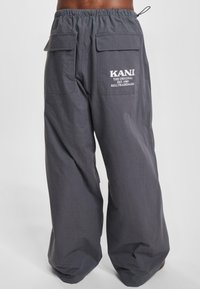 Šedé kalhoty s širokými nohavicemi a elastickým pasem. Obsahují dvě velké zadní kapsy a bílé logo na pravé kapse.