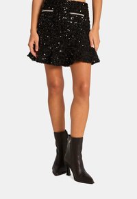 Zwarte flonkerende flared rok met een gerimpelde onderkant, voorzien van twee zakken en strass accenten. Gecombineerd met puntige zwarte enkelboots.