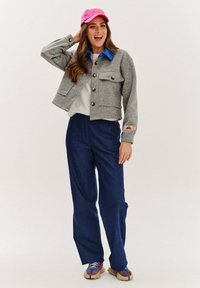 Šedá vlnená bunda s gombíkovým zapínaním, modrým golierom a dvoma prednými vreckami. V kombinácii s námorníckymi nohavicemi so širokými nohavicami a viacfarebnými sandálmi. Rúžová čiapka.