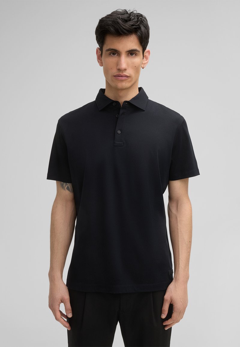 Czarny polo wykonany z gładkiego materiału, z kołnierzykiem i zapięciem na trzy guziki. Krótkie rękawy i luźny fason.