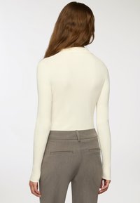 Biała, prążkowana bluzka z długim rękawem i kołnierzykiem, zestawiona z szarymi spodniami o wysokim stanie z tylnymi kieszeniami i gładką fakturą.