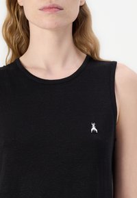 Juodas be rankovių marškinėlis, pagamintas iš minkštos medvilnės, su apvalia iškirpte. Yra mažas sidabrinis emblem tik kairėje krūtinės pusėje. Lygus paviršius.