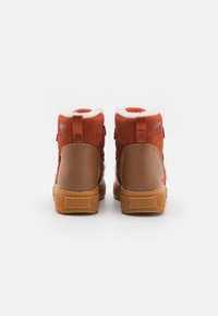 Botines de ante rojo con forro de pelo sintético blanco y suelas de goma marrón. Presentan un logo en la parte trasera y dos lengüetas para facilitar su uso.