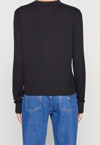 Jersey negro de punto con un cinturón y puños acanalados, que presenta un detalle en forma de V en la parte posterior. Combinado con jeans de mezclilla azul claro.