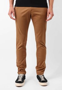 Pantalons en mélange de coton beige avec une coupe slim, présentant une texture lisse et un design classique à cinq poches. Associés à des baskets noires.