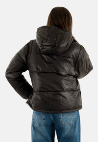 Giacca a vento nera con cappuccio, caratterizzata da un design trapuntato e polsini elasticizzati, abbinata a jeans di denim blu.