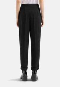 Pantaloni neri a vita alta con taglio morbido, pieghe e risvolti, abbinati a scarpe nere lucide. Tessuto liscio, design minimalista.