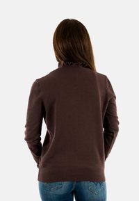 Maglione marrone con un motivo testurizzato, collo a volant e maniche lunghe, abbinato a jeans blu, visto da dietro.