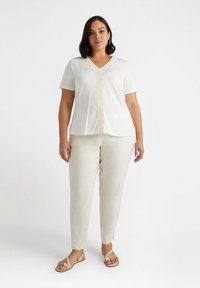 Top blanco de manga corta con escote en V y un borde de encaje ondulado decorativo en el frente. Combinado con pantalones beige claros y sandalias.