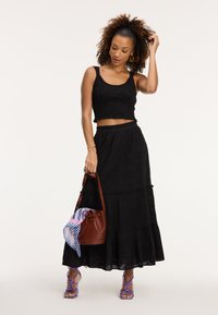 Čierny cropped top s volánovým okrajom, ktorý je skombinovaný s čiernou tiered sukňou s kvetinovou výšivkou. Hnedá vedierková taška so vzorovaným šatkou a fialovými sandálmi na opätku.