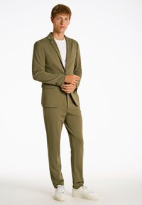 Olivgrüner Anzug mit einem Ein-Knopf-Blazer und schmal geschnittenen Hosen, kombiniert mit einem weißen T-Shirt und weißen Sneakers. Reines Gewebe und maßgeschneiderte Design.