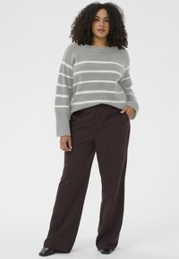 Sivý pásikavý sveter s dlhými rukávmi, rebrovaným výstrihom, v kombinácii s tmavo hnedými širokými nohavicami a čiernymi topánkami. Hladké textúry po celom oblečení.
