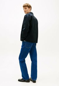 Zwarte casual jas met lange mouwen, gecombineerd met blauwe denim jeans. De jas heeft een eenvoudig ontwerp en de jeans hebben klassieke achterzakken.