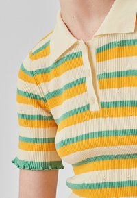 Polo à côtes avec des rayures horizontales jaunes, vertes et crème, doté d'un col classique et d'ourlets à volants aux manches.