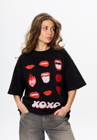 Zwarte oversized T-shirt met verschillende rode lippenafbeeldingen en het woord "xoxo" in vet witte letters op de voorkant. Gemaakt van katoen.