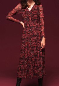 Långärmad klänning i genomskinligt svart tyg med röd blommig paisleymönster, med V-ringning och åtsittande midja, som flödar ner till anklarna.