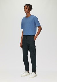 Blauwe T-shirt met korte mouwen en ronde hals, gecombineerd met zwarte cargobroek met zijzakken en elastische boorden, gedragen met witte sneakers.