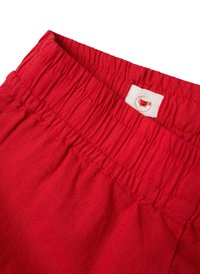 Röda shorts med elastisk midja, tillverkade av bomull. Har struktur av samlad textur och en vit tagg med en röd accentknapp.