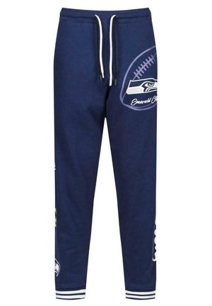 Pantalon de survêtement bleu marine avec cordon blanc, arborant un graphique de football et le logo de l'équipe sur la jambe droite. Poignets côtelés aux chevilles.