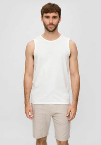 Weiße ärmellose Tanktop aus leichtem Stoff, kombiniert mit beigen Shorts, die zwei Vordertaschen und ein schlichtes Design aufweisen.