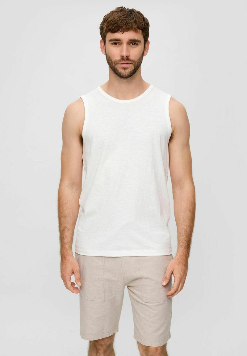 Weiße ärmellose Tanktop aus leichtem Stoff, kombiniert mit beigen Shorts, die zwei Vordertaschen und ein schlichtes Design aufweisen.