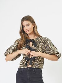 Blusa cropped con stampa leopardata, caratterizzata da maniche a sbuffo, un'apertura frontale a chiave con dettagli in legno neri, realizzata in tessuto morbido. Abbinata a jeans neri.