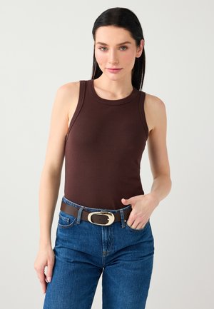 Haut marron sans manches en tissu côtelé, associé à un jean en denim bleu et une ceinture marron avec une boucle dorée. Design simple et ajusté.