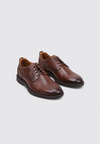 Zapatos de cuero marrón con un acabado suave, diseño de cordones, punta redondeada y un interior en un tono marrón claro que contrasta. Suela de goma.