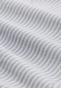 Närbild av vitt tyg med tunna, jämnt fördelade svarta vertikala ränder och mjuka veck som skapar en vågig textur.