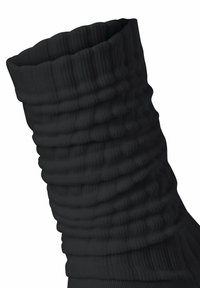 Schwarze gerippte Socke mit einem breiten, strukturierten Bündchen. Das Material wirkt weich und elastisch und weist auffällige horizontale Rillen auf.