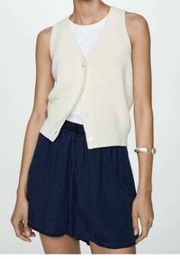 Cárdigan sin mangas de punto en color crema con escote en V y botones delanteros, combinado con una falda azul marino con cordón en la cintura. Textura suave, ajuste casual.
