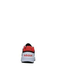 Sneaker bianco e nero con accenti rossi. Presenta un collo e una linguetta imbottiti in rosso, il logo "adidas" sul tallone e una tomaia texture.