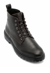 Bottine en cuir marron avec bout rond, œillets métalliques et semelle en caoutchouc texturée, équipée d'une boucle au talon pour faciliter l'enfilage.