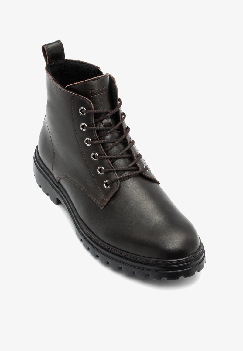 Bottine en cuir marron avec bout rond, œillets métalliques et semelle en caoutchouc texturée, équipée d'une boucle au talon pour faciliter l'enfilage.