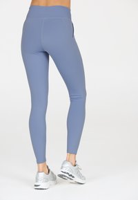 Blå leggings i stretchigt material med hög midja, med en sidoficka, kombinerade med silverfärgade träningsskor.