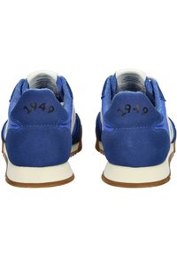 Scarpe da ginnastica in suede blu con accenti bianchi, caratterizzate dalla scritta "1949" impressa sul tallone e una suola in gomma texturizzata per una migliore aderenza.