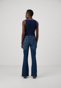 Marineblå ermeløs topp kombinert med lyseblå vide jeans. Outfiten har en slim fit, denimtekstur og doble baklommer.