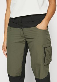 Kargo bikses ar melnu elastīgu jostasvietu, olīvzaļas krāsas audumu ar tekstūrētu apdari, sānu kabatām un ar rāvējslēdzēju aizvērtu kargo kabatu.