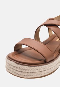 Sandal in pelle marrone con tre larghe cinghie e una suola piattaformata intrecciata naturale e testurizzata. Interno liscio con soletta imbottita.