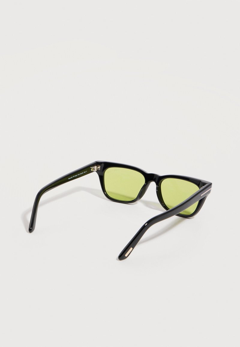 Lunettes rectangulaires noires avec montures fines et verres teintés jaunes, posées ouvertes sur une surface blanche.