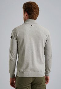 Grauer gestrickter Pullover mit hohem Kragen, gerippten Bündchen und Saum. Auffälliges Logo-Detail im Nackenbereich; glatte Textur und figurbetontes Design.
