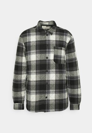 Chemise en plaid noir, blanc et gris avec un design à boutons, manches longues, poche poitrine et texture matelassée. Dispose d'un col arrondi.