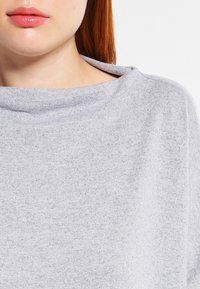 Grauer, leichter Pullover mit einem Boot-Ausschnitt-Design. Glatte Textur mit einem dezenten Strickmuster. Akzente sind ein gefalteter Kragen.